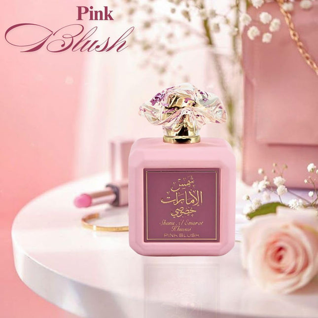 Pink perfume bottle with 'Pink Blush' branding on a pink background with flowers and jewelry.