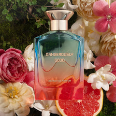Perfume bottle labeled 'Dangerously Good' surrounded by flowers and a sliced grapefruit.