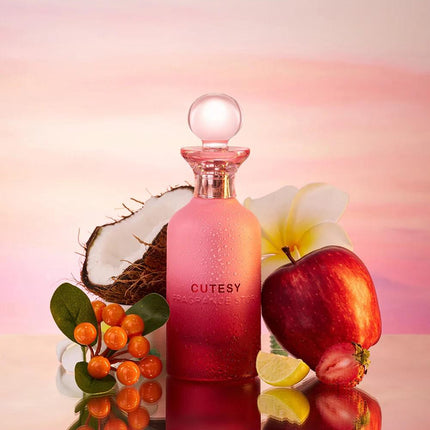 Pink bottle labeled 'CUTESY' surrounded by fruits and flowers on a reflective surface with a gradient background.